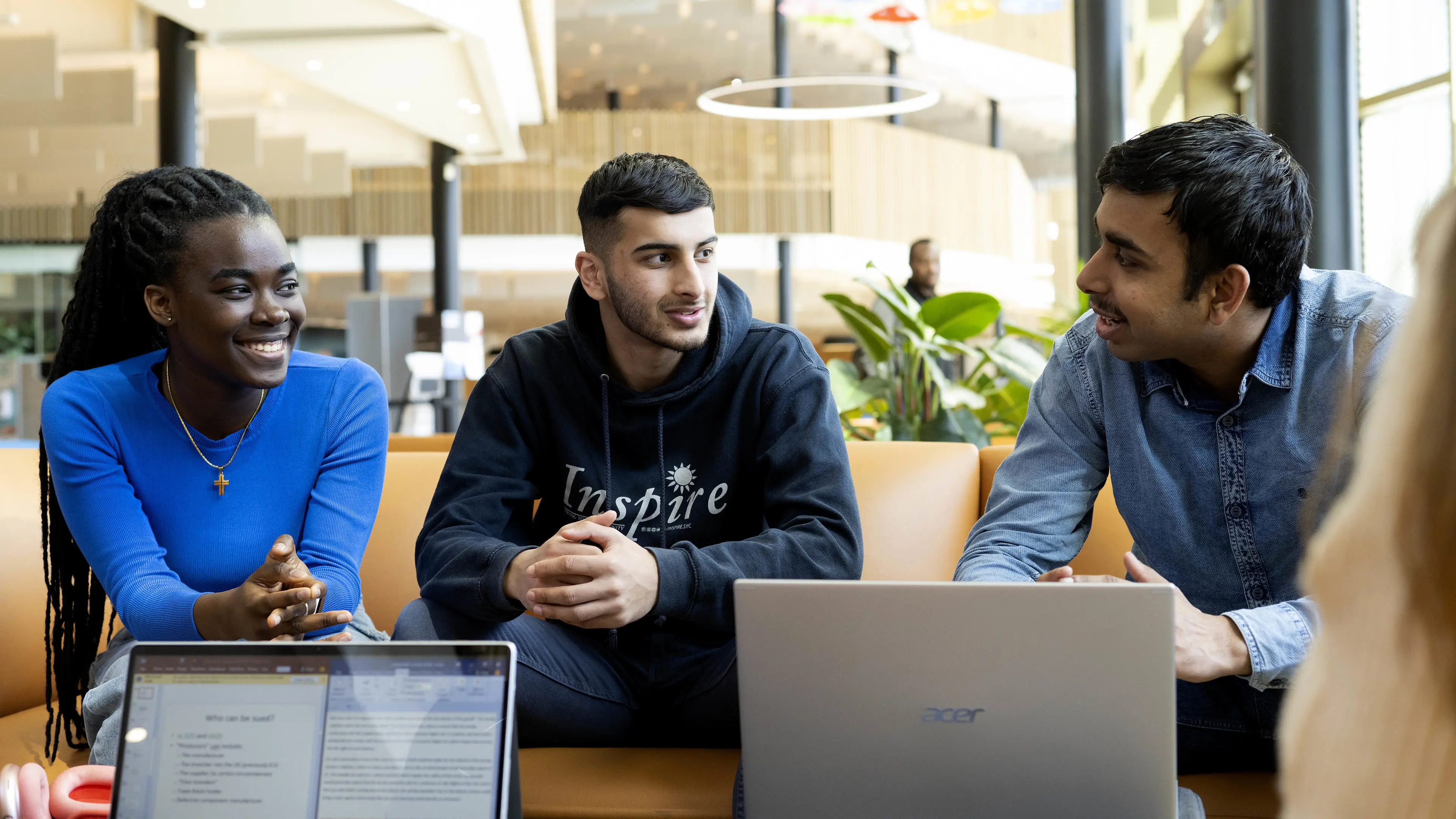 A group of students sit on a sofa with laptops, chatting to one another.