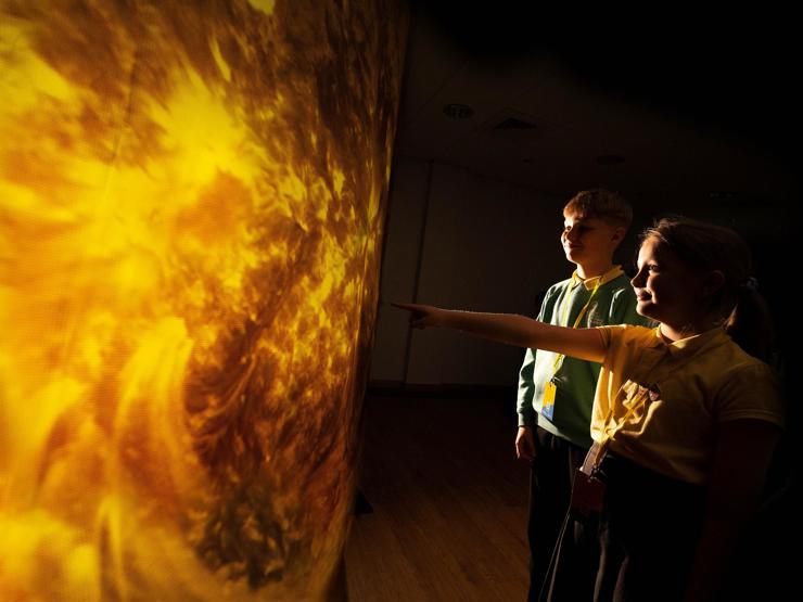 Two primary school students reach out to touch a model of the sun.