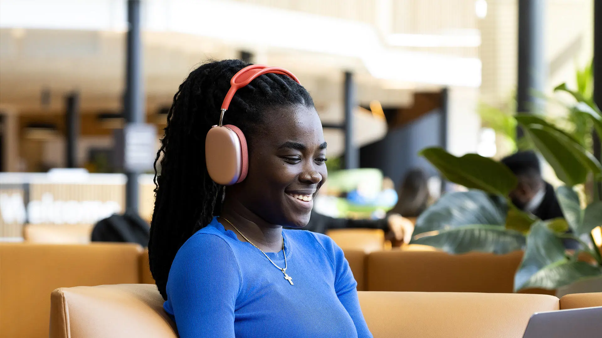 student sat on an orange sofa in the student centre looking at a laptop wearing headphones
